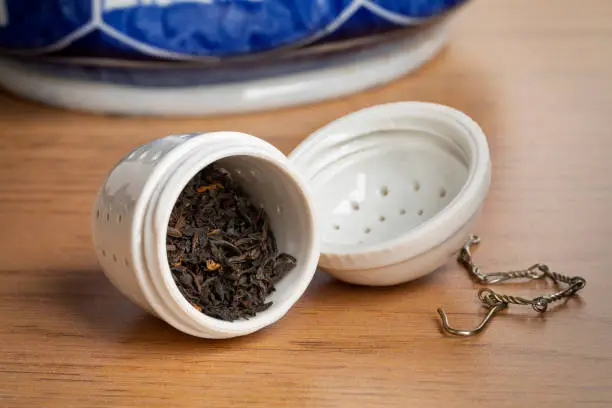 White ceramic open tea strainer with dried Chinese Kee Mun tea leaves close up to start making tea