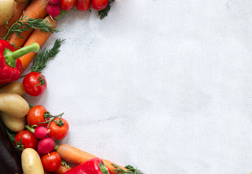 Healthy food backgrounds: multicolored fresh organic root vegetables shot from above on rustic wooden table. Root vegetables included in the composition are carrots, radish, onion, potatoes, garlic, ginger and turmeric. Some dirt is visible under the vegetables. The composition is at the right of an horizontal frame leaving useful copy space for text and/or logo at the left. High resolution 42Mp studio digital capture taken with SONY A7rII and Zeiss Batis 40mm F2.0 CF lens