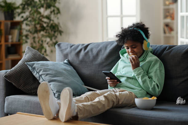 istock Cute youngster in pants and sweatshirt sitting on sofa and watching video 1473173415