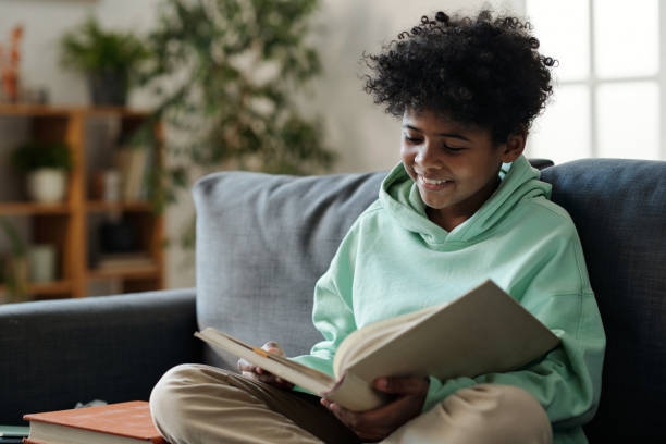 istock Smiling schoolboy in casualwear reading book while sitting on couch 1473173433