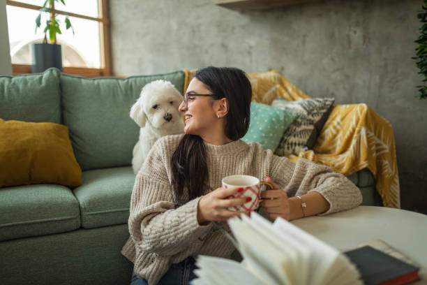 istock Young woman drinking tea while playing with her dog at home 1473173642