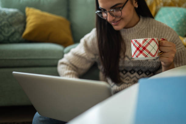 istock Young woman using a laptop and drinking tea at home 1473173955