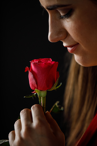 Profile view of happy young woman in love holding and smelling a single red rose she received from a loved one for Valentine's day.