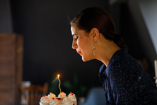 Profile view of joyful young woman blowing out the birthday candle on a cake after making a wish.