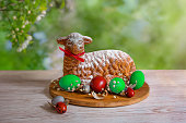 Easter pastries on the table with colorful eggs on the background of a blooming spring garden. A traditional treat for Easter. The Lamb of God.