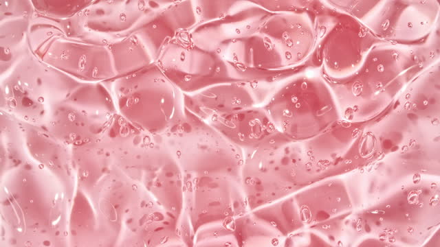 Pink Transparent Cosmetic Gel Fluid With Molecule Bubbles Flowing On The Plain White Surface. Macro Shot