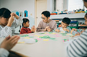 An Asian preschool teacher is guiding the children in doing a handicraft activity.