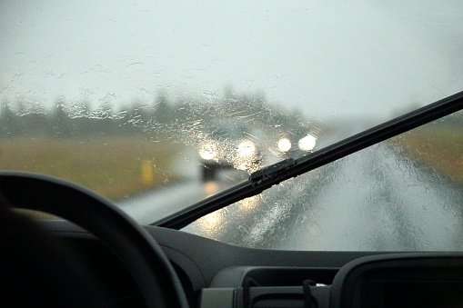 Driving a car in the rain with activated windshield wipers, traffic.