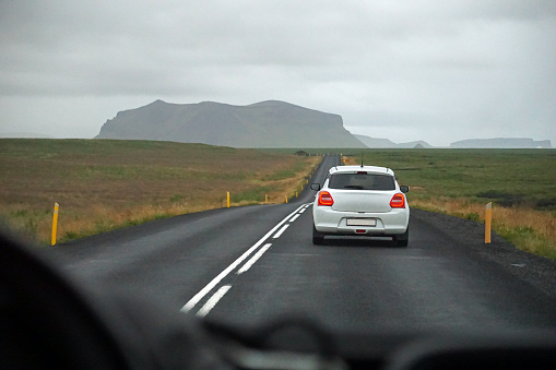 Driving a car in Iceland - perspective of a driver, mountain range in a distance, traffic.