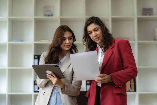 istock Two young cheerful businesswoman working using digital tablet at conference table with work papers at office. Female business colleague using touch screen computer for real estate project discussion 1473181607