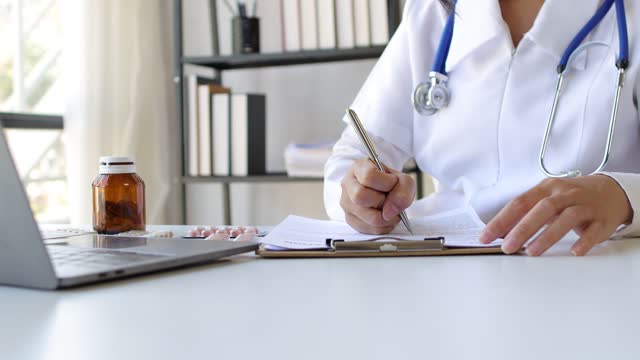 Female doctor or pharmacist working in a hospital is writing a prescription in the doctor's office.