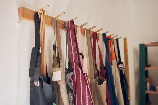 Clothing rack, apron and workshop of clothes hanging on a creative studio wall for art, style or design. Closeup of aprons or work equipment for artistic development on rack for business startup