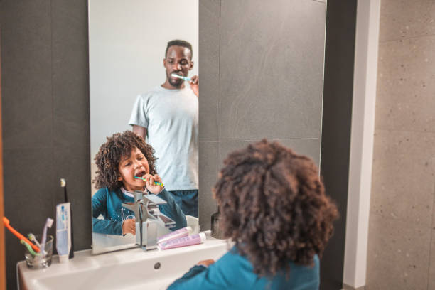 istock Cool African-American Boy Brushing Teeth With Dad Watching Him 1473186399