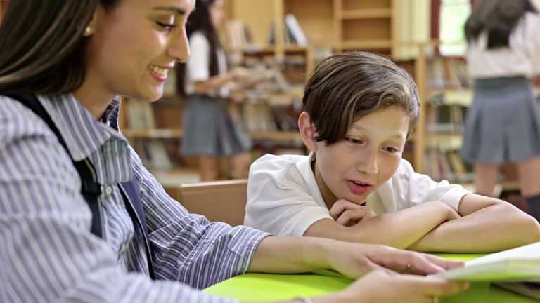 Educator and Hispanic schoolboy reading together