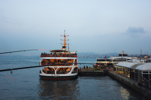 Istanbul, Turkey 11.25.2019 The ferry that picks up its passengers at Karaköy Pier in Istanbul and the fishing rods of the fishermen on the Galata Bridge