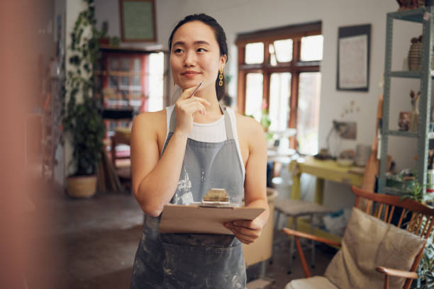 istock Creative woman, workshop and thinking with clipboard, design or vision for schedule, strategy or ideas. Asian artist, small business owner and studio for art idea art, checklist or focus in workspace 1473193053