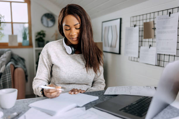 istock Young beautiful casually clothed woman taking notes while studying from her apartment 1473193189