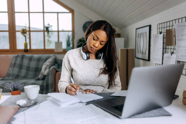 istock Young beautiful casually clothed woman taking notes while studying from her apartment 1473193199