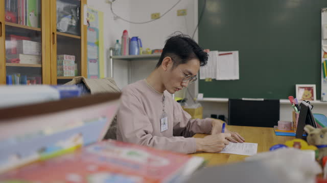 An Asian Chinese male school teacher is sitting at his desk in his workplace, drafting his upcoming teaching plans.