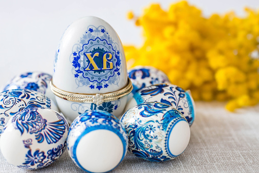A large egg box with the inscription XB, mimosa and Easter eggs in traditional Russian style on a linen tablecloth on the table. Gzhel. The concept of a bright Easter holiday.