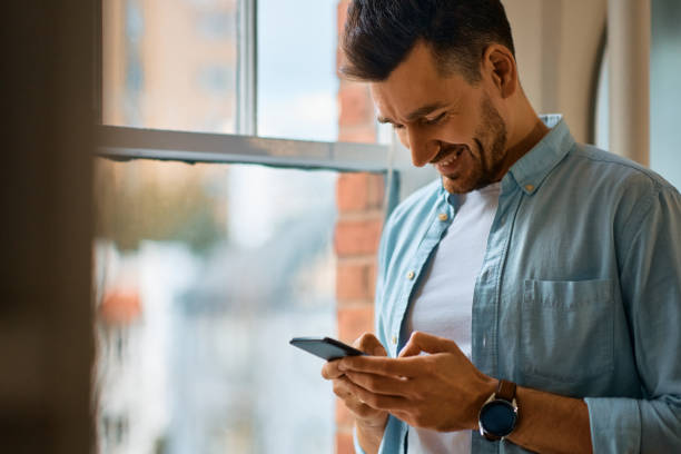 istock Happy man text messaging on smart phone by the window. 1473198675
