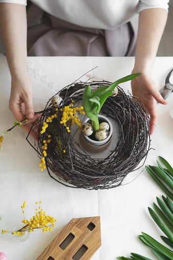 Easter wreath diy with woman hands, flowers on table, handicraft, artisanal, springtime concept, top view