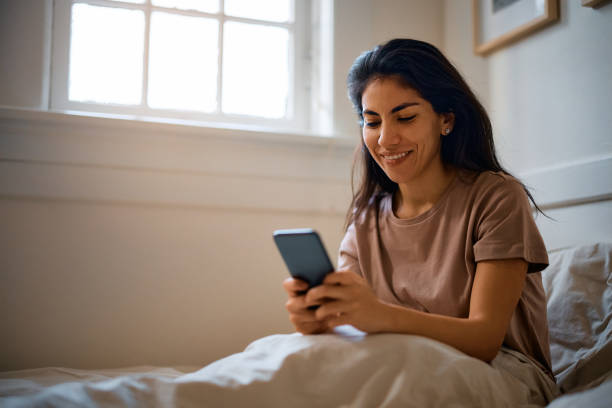 istock Happy woman text messaging on cell phone in bedroom. 1473199718