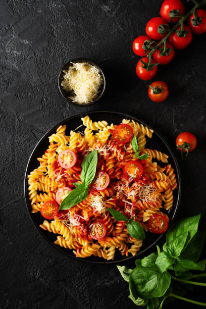 istock Fusilli pasta with tomatoes, basil, parmesan, and sauce on back background 1473199755