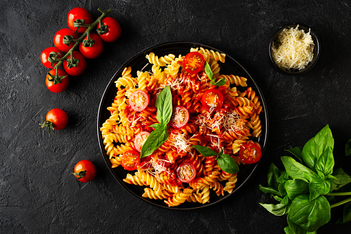 Fusilli pasta with tomatoes, basil, parmesan, and sauce on back background, top view, close up
