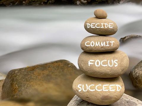 Inspirational and motivational words of decide commit focus succeed on stones with vintage background.