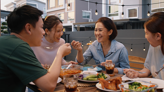 Mom enjoy thai meal cooking for family day meet talk home dining at dine table cozy patio. Group asia people young adult man woman friend fun joy relax warm night time picnic eat yummy food with mum.