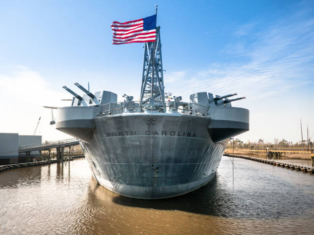 Stern of the battleship USS North Carolina, docked in Wilmington, NC.  Name of the ship in bold lettering with full American flag blowing in the breeze. stock photo