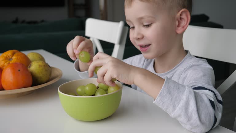 Boy Picks Berries With Hands Green Grapes At Kitchen Table Juicy Fruits