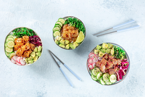 Poke bowl, healthy Hawaiian dish, variety. Plates with salmon, tuna, and shrimps, overhead flat lay shot with chopsticks