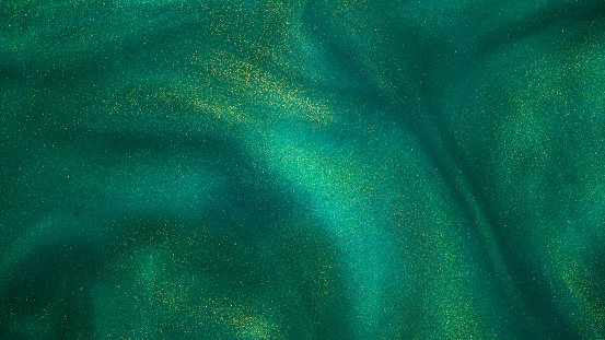 Abstract magic green background with golden sparkles. Photo of a green liquid with different depth of field and gold glitters. Various shades of green with golden splashes. Green backdrop with tints of golden glitters.