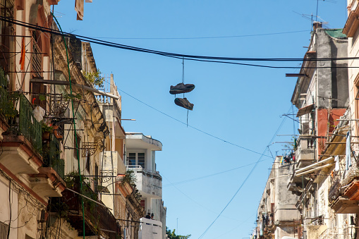 Havana, Cuba - January 20, 2023: Low-angle view of building facades with wires crisscrossing the street. A pair of shoes is hanging from one of the cables by their laces.