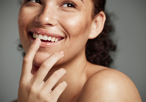Woman, sugar scrub and lips with smile for skincare, makeup or cosmetics against a grey studio background. Happy female smiling in happiness for facial cosmetic, lip dermatology or mouth exfoliation