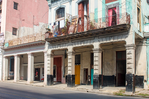 Havana, Cuba - January 23, 2023: Facade of a story building with pillars and balconies. A clothesline is on one of the patios, and incidental people are on the ground floor.