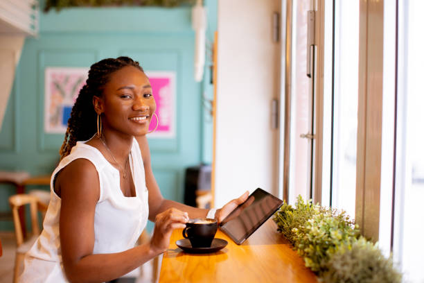 istock Young black woman drinking coffee while looking at digital tablet in the cafe 1473206893