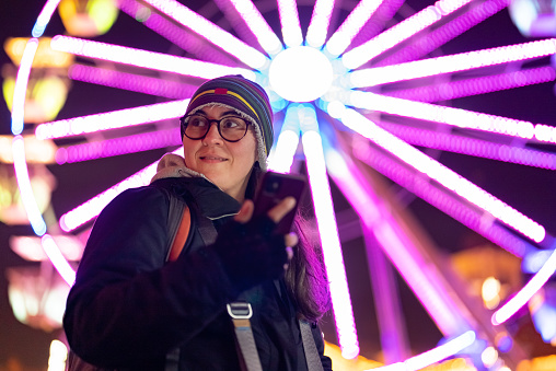 Woman using smartphone in front of ferris wheel