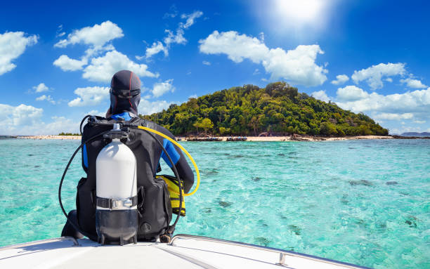 A scuba diversits on a boat and looks at the turquoise sea in Krabi, Thailand A scuba diver in his diving gear sits in front of a boat and enjoys the view of the tropical landscape with turquoise sea in Krabi, Thailand diving equipment stock pictures, royalty-free photos & images