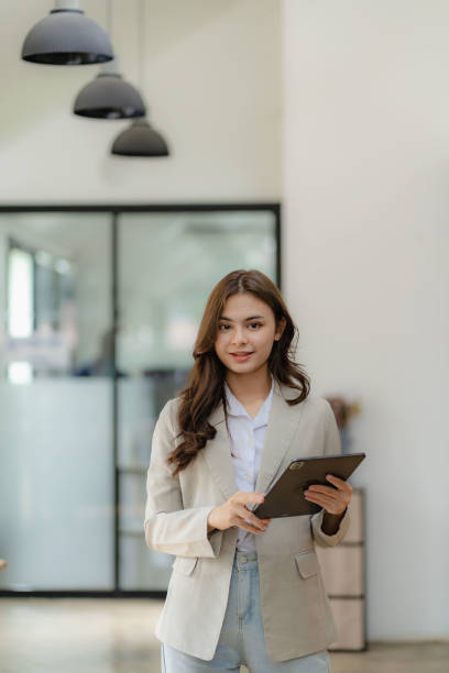 istock Young female employee standing holding tablet smiling looking at camera in office vertical image 1473211871