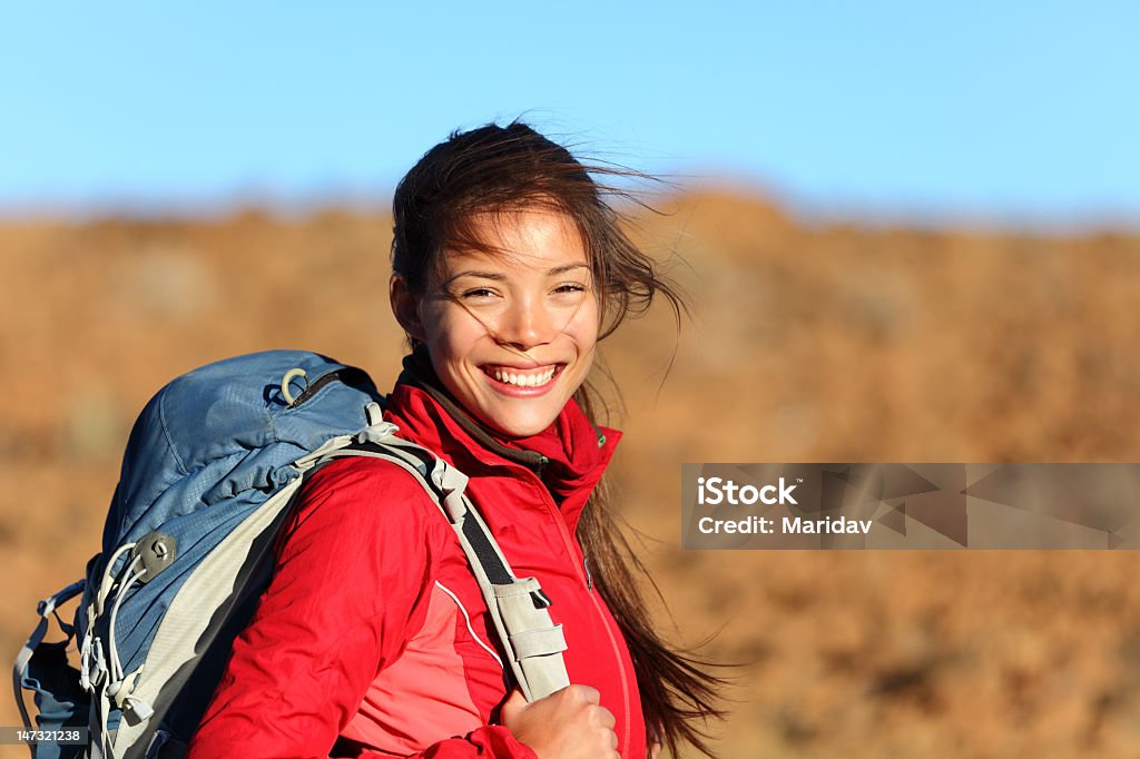 Young woman with a backpack smiling at camera Healthy lifestyle xwoman hiker smiling happy outside on hiking trip. Beautiful natural candid smile on mixed race Caucasian / Asian female hiker outdoors in nature. Hiking Stock Photo