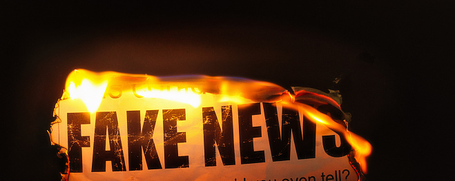 Burning simulated newspaper clipping sows doubt about fake news.