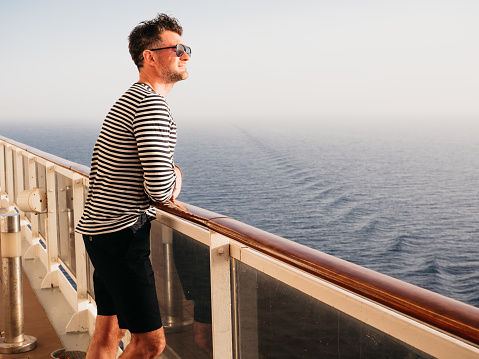 Handsome man standing on the empty deck of a cruise ship. Sunny morning, clear day. Closeup, outdoor. Vacation and travel concept
