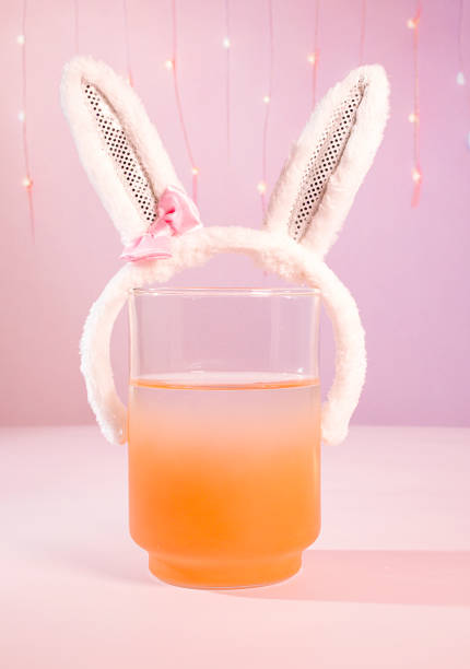 istock Easter Drinks & Beverages: A Pastel Orange and Pink Dreamy Beverage Cocktail with Furry White Bunny Rabbit Ears on a Pink Background with Festive Party Lights 1473215730