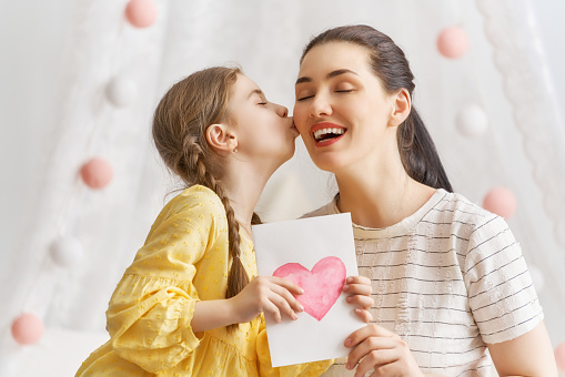 Happy women's day! Child daughter is congratulating mom and giving her postcard. Mum and girl smiling and hugging. Family holiday and togetherness.