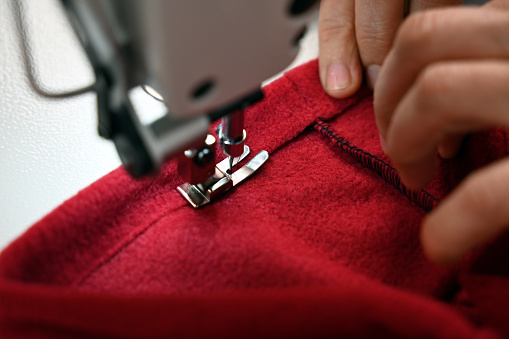 Close-up of woman hand sewing red fleece fabric on the sewing machine.