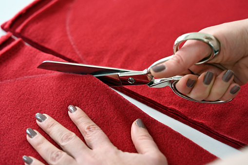 Close-up of tailor cutting red fabric with scissors
