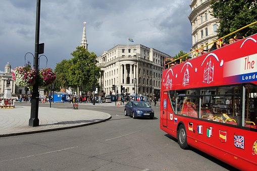 London, England - August 27, 2011: Double-decker buses drive around Trafalgar Square traffic circle, a popular travel destination in the UK. The bus is filled with identifiable tourists on a bus tour of the city.